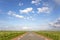 Road with red cycle path on both sides, perspective, sky with clouds and a faraway straight horizon