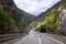 Road in rocky mountains in spring. Beautiful mountain curved roadway, trees with green foliage and overcast sky. Traveling trough