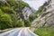 Road in rocky mountains in spring. Beautiful mountain curved roadway, trees with green foliage and overcast sky. Traveling trough