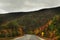 The road running among the mountains overgrown with autumnal bright forest and dramatic sky.White Mountain National Park. USA. New