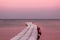 Road in the sea. Wooden Pier, leaving the horizon of the ocean. Water on the sunset. Landscape in natural lilac sun