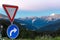 Road sign give way to alpine mountains background.