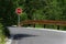 Road sign on a metal pole `STOP` with forest behind the sign and guard rail on the side of the road.