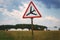 Road sign with red triangle and black plane going down landing standing in the field on blue sky background with clouds