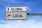 Road sign with words global and local. White two street signs with arrow on metal pole on blue sky background