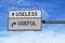 Road sign with words useless versus useful. White two street signs with arrow on metal pole on blue sky background