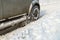 Road snow flies up from a vehicle's spinning wheel. Car's wheels spin and spew up pieces of snow it attempts to gain