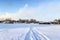 Road on snow and ice of frozen lake, tracks going to village, sunny cold weather