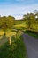 Road to white house, green meadows and trees.