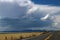 Road trip - Black top two lane highway stretches over the horizon past a barn and hay field by a lake towards the distant mountain