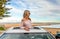 Road trip summer beach vibes.  Carefree woman in sunroof car by beach