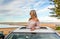 Road trip to beach. Carefree woman in sunroof with views