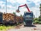 Road truck is loading the railway heavy wagon with spruce trunks