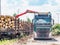 Road truck is loading the railway heavy wagon with spruce trunks