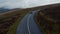 Road winding through large moorlands. Tracking of vintage sports car driving on wet road on cloudy day. Ireland