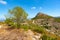 Road winding through mountains toward to rock outcrop at summit past ancient stone-walled terraces on Coll de Rates