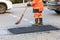 A road worker collects fresh asphalt with a panicle on the part of the road being repaired