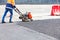 A road worker compacts asphalt with a gasoline vibratory compactor