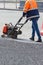 A road worker compacts fresh asphalt with petrol vibratory plate on a sunny day