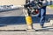 A road worker operates a vibratory rammer to fill the road with asphalt