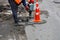 A road worker smashes asphalt with an electric jackhammer around a sewer hatch on the road