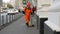 A road worker in uniform sweeps trash on the sidewalk. Janitor in orange overall