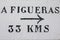 Roadsign on white wall with arrow pointing to Figueras at 33 km, Spain