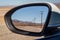 Roadway in Mojave Desert of American southwest in rear view mirror. Electric wooden poles along the road