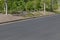 Roadway by parking lot, asphalt with formed concrete curb, trees and bushes landscaping