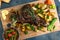 Roast shoulder of lamb on baked potato and carrots, wooden board, top view