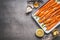 Roasted Baby Topped carrots on baking sheet with thyme, honey, garlic and lemon on gray concrete background, top view, border.