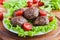 Roasted beef cutlets, green salad and small tomatoes on white plate