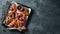 Roasted chicken wings in barbecue sauce with sesame seeds and parsley in a baking tray on a dark table. Top view with copy space.