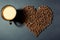 Roasted grains in the shape of a heart and a cup of aromatic coffee on a table