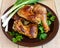 Roasted juicy chicken (legs, winglets) on a clay plate on a light wooden background.