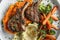 Roasted lamb chops with a side of mashed sweet potato and steamed vegetables. The steamed vegetables are a mix of broccoli and