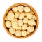 Roasted macadamia nuts in wooden bowl over white