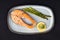 Roasted salmon steak with asparagus in a plate on dark background