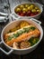 Roasted salmon steak with roast potatoes and tomatoes served in ceramic pan on wooden table