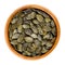 Roasted salted pepita pumpkin seeds in wooden bowl over white