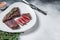 Roasted sliced rump beef meat steak on a plate with thyme. White background. Top view. Copy space