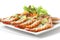Roasted sliced tiger shrimps with baked potato, slice of lemons, vegetables & chili sauce on square plate, isolated on white