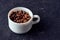 Roasted whole coffee beans in white porcelain cup on gray textured background