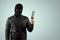 Robber, bandit in a balaclava with a phone in his hands on a light background. Robbery, hacker, crime, theft. Copy space