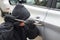 Robber man in black hoodie jacket using a crowbar to break lock and steal a vehicle. Car thief or theft for insurance concept
