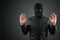 Robber, a thug in a balaclava raised his hands on a black background, surrenders. Robbery, hacker, crime, theft, arrest. Copy