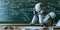 Robot Sitting at Desk in Front of Chalkboard