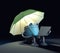 The robot sitting under umbrella and looks at the screen of the laptop