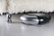 Robot vacuuming under sofa. Black and silver robotic vacuum cleaner on white laminate floor