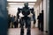 Robot Walks Down Office Corridor, With Unfocused People In Business Suits Sitting In The Background. The Concept Of Replacing